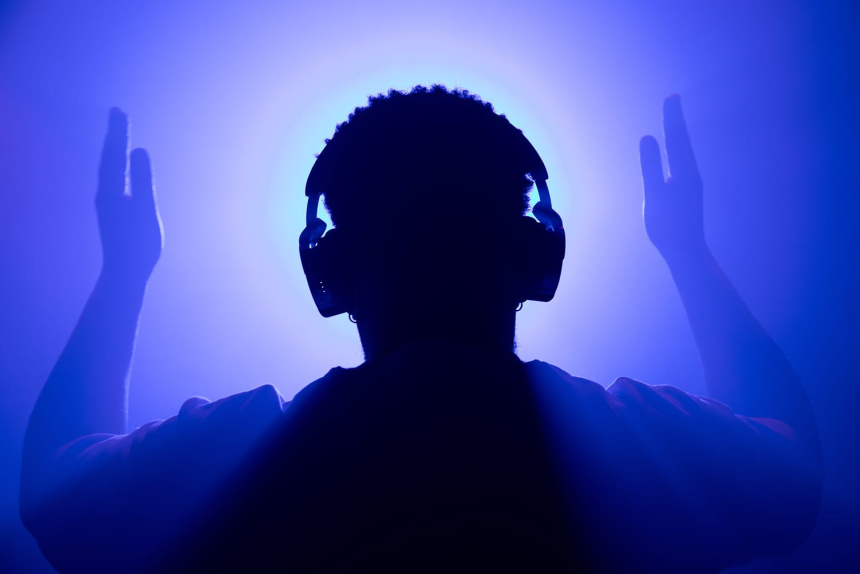 Silueta de una persona con auriculares y brazos levantados frente a luz azul y violeta