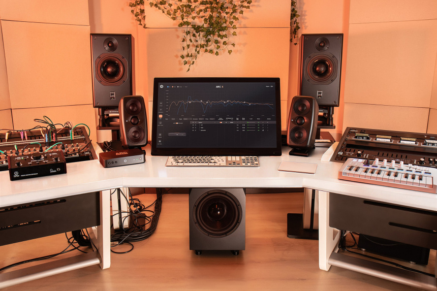 ARC Studio+ sobre una mesa de estudio junto a dos pares de monitores, un subwoofer y sintetizadores